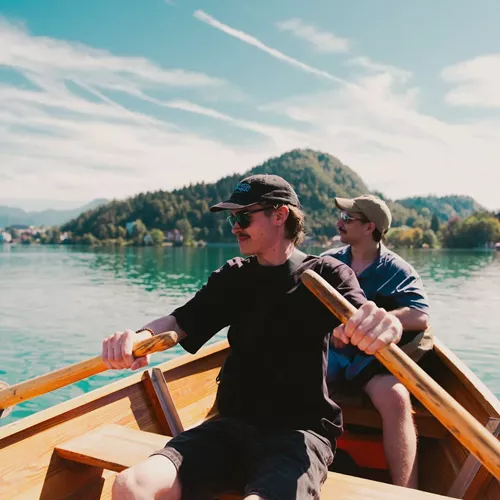 Travellers take in stunning mountain views while rowing across an emerald lake on the Contiki Budapest to Dubrovnik Tour