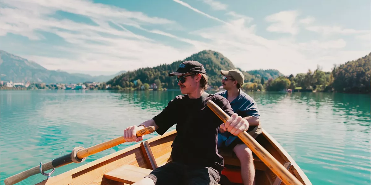 Travellers take in stunning mountain views while rowing across an emerald lake on the Contiki Budapest to Dubrovnik Tour