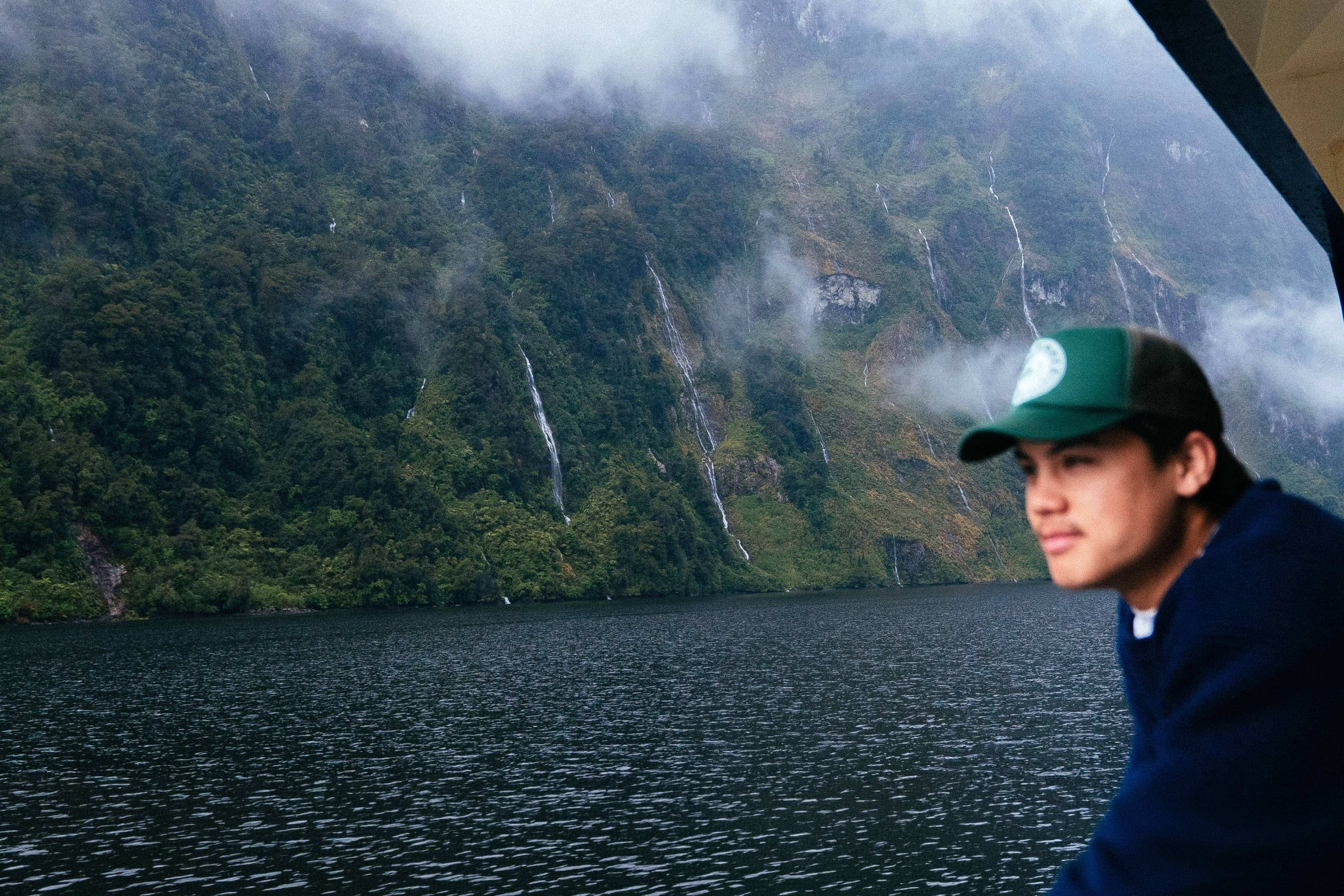 View of waterfalls cascading into Milford Sound from a boat in Fiordland National Park, New Zealand.