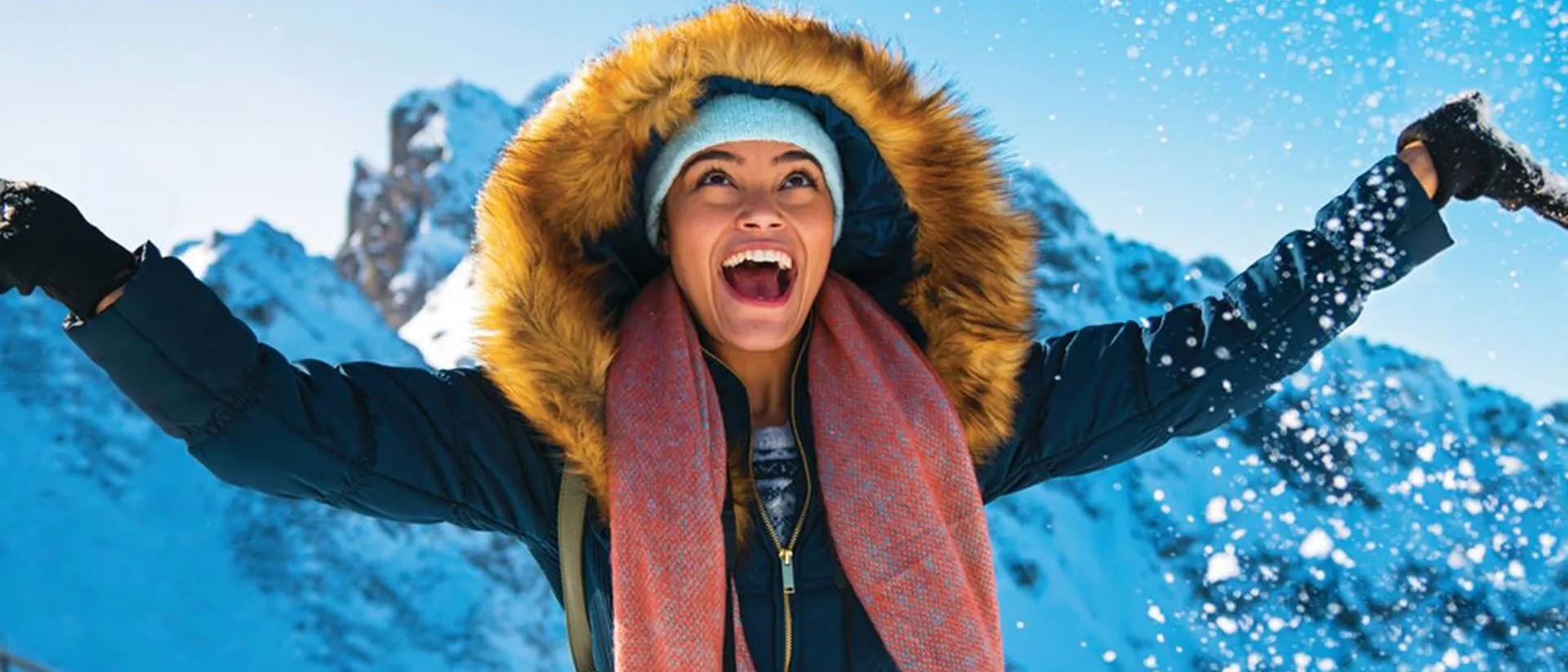 Happy woman in warm clothes catching snow on mountain top in Swiss Alps, Switzerland