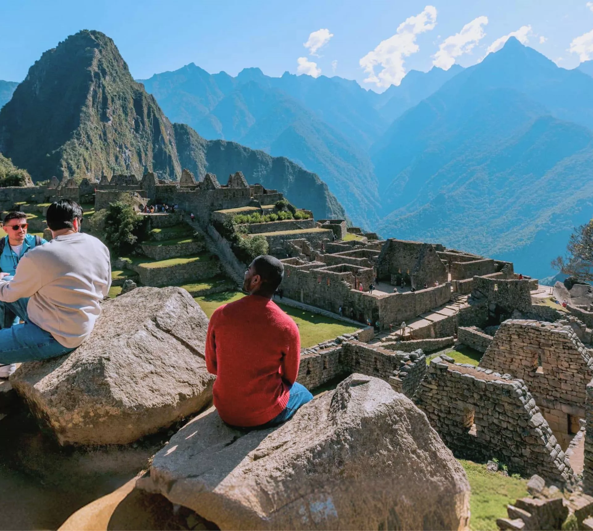 Group of young Contiki travellers sitting on rocks overlooking the ancient Inca ruins of Machu Picchu with Huayna Picchu mountain in the background Peru - Contiki South America Lima to Rio Tour