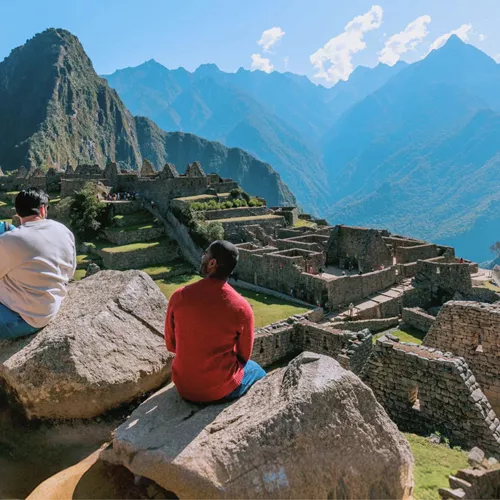 Group of young Contiki travellers sitting on rocks overlooking the ancient Inca ruins of Machu Picchu with Huayna Picchu mountain in the background Peru - Contiki South America Lima to Rio Tour