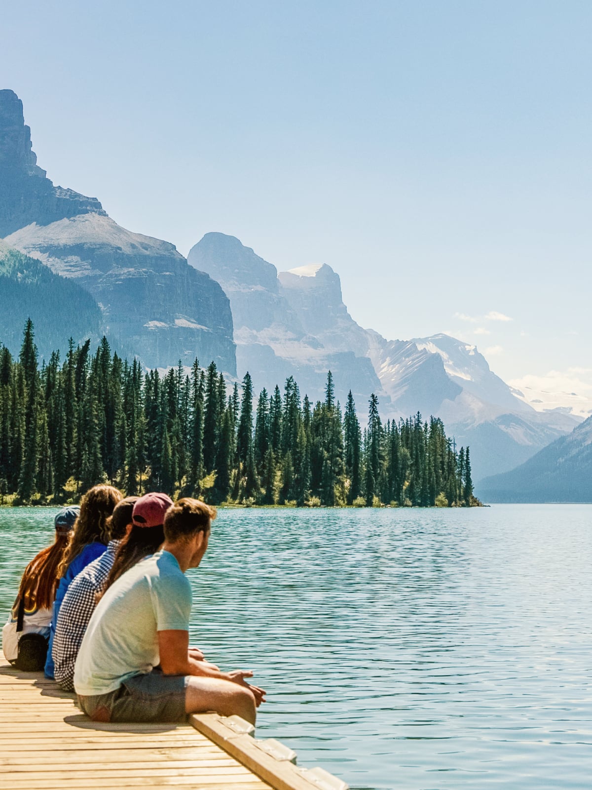 Travellers sitting on a dock overlooking a turquoise lake and Rocky Mountains in Canada.