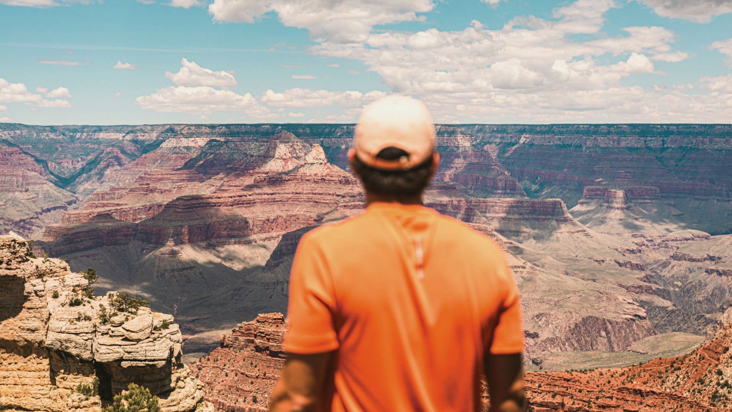 Traveller in an orange shirt overlooking the vast canyon landscape at Grand Canyon National Park, Arizona, USA.
