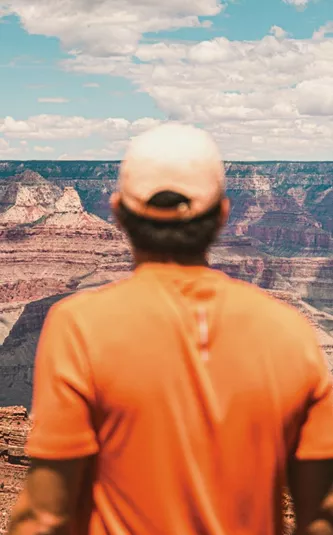 Traveller in an orange shirt overlooking the vast canyon landscape at Grand Canyon National Park, Arizona, USA.