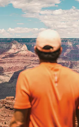 Traveller in an orange shirt overlooking the vast canyon landscape at Grand Canyon National Park, Arizona, USA.