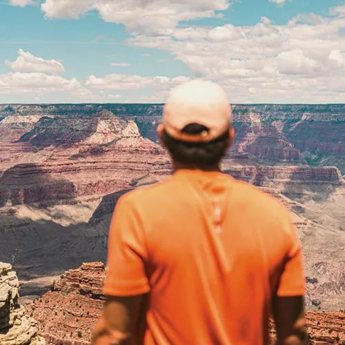Traveller in an orange shirt overlooking the vast canyon landscape at Grand Canyon National Park, Arizona, USA.