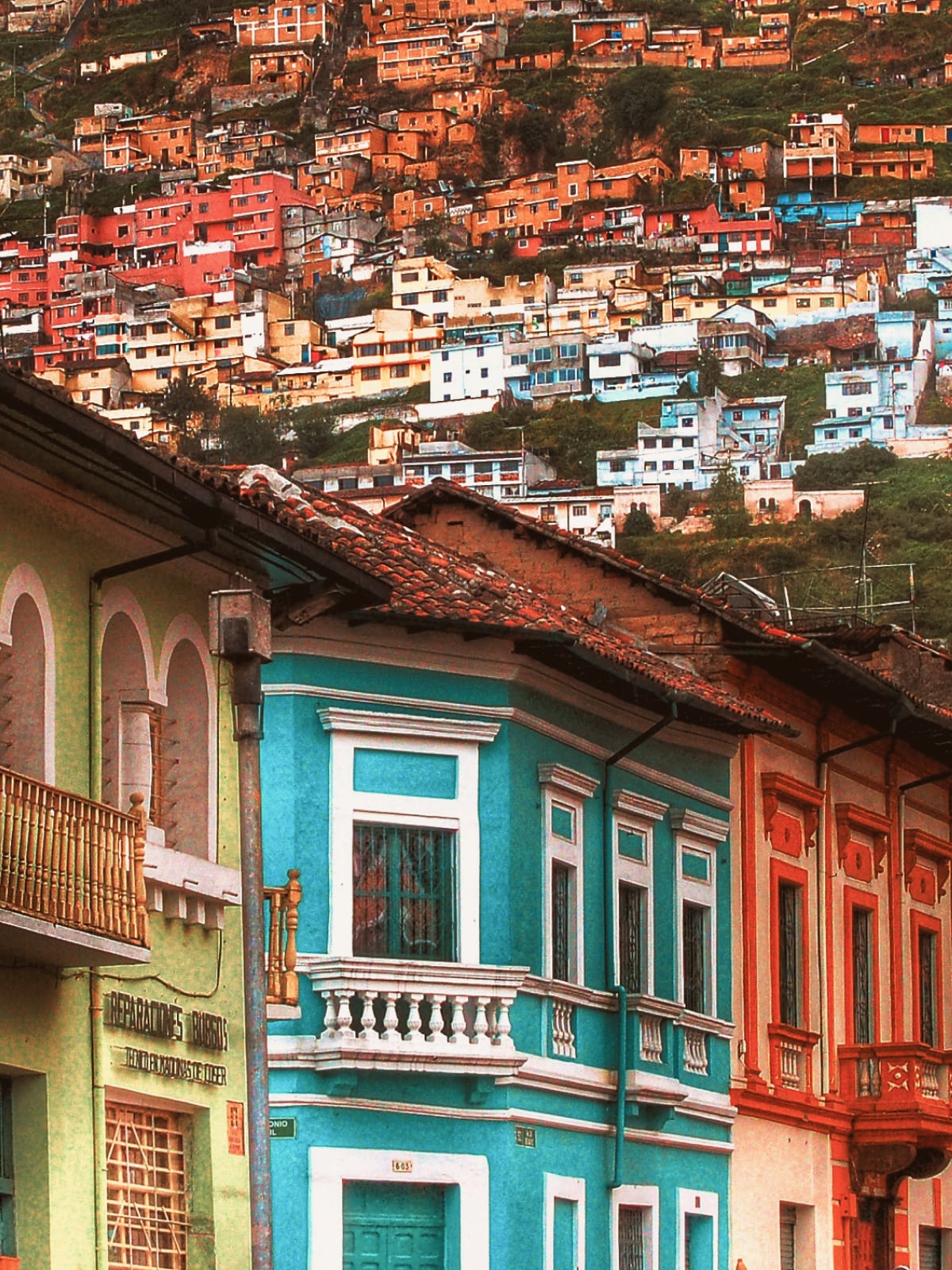 Colourful colonial buildings in Quito's old town with hillside houses climbing the slope behind, Ecuador.
