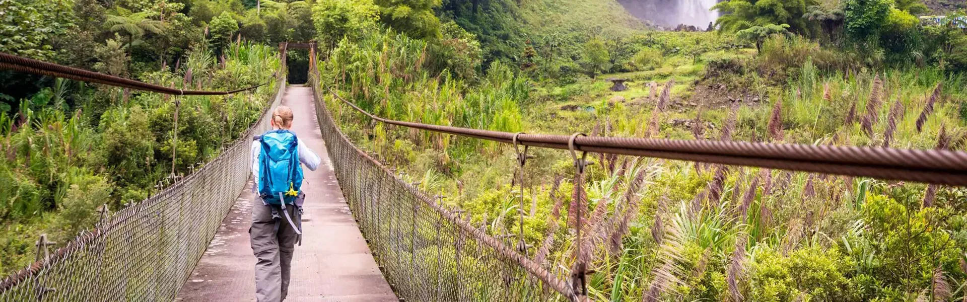 A woman crossing a narrow bridge with nature around her in Ecuador.