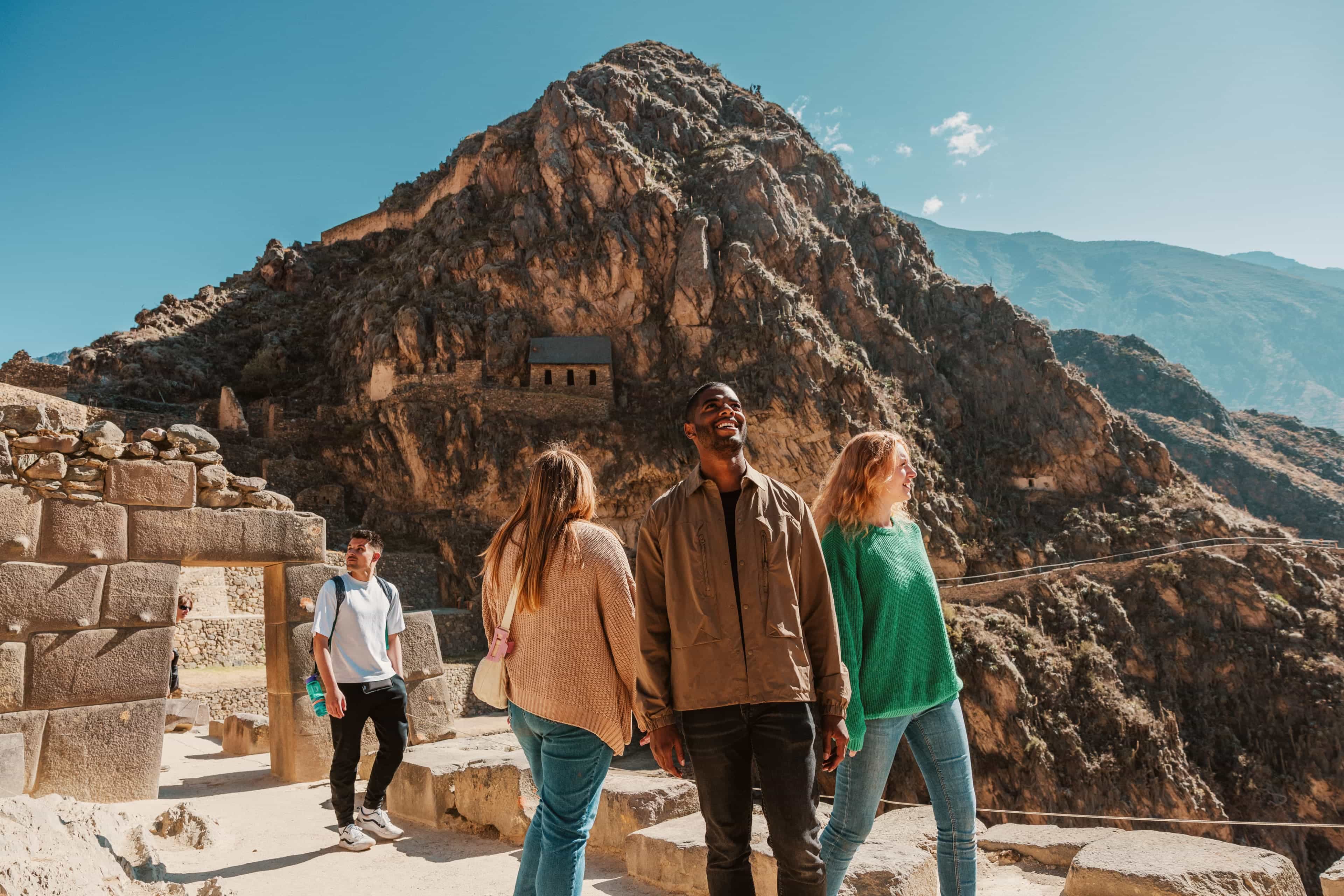 Travellers exploring the Inca ruins of Ollantaytambo, Peru, with terraced ruins rising up the mountainside behind them.