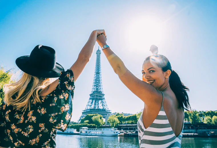 Two female travellers raising their hands and admiring the Eiffel Tower, Paris