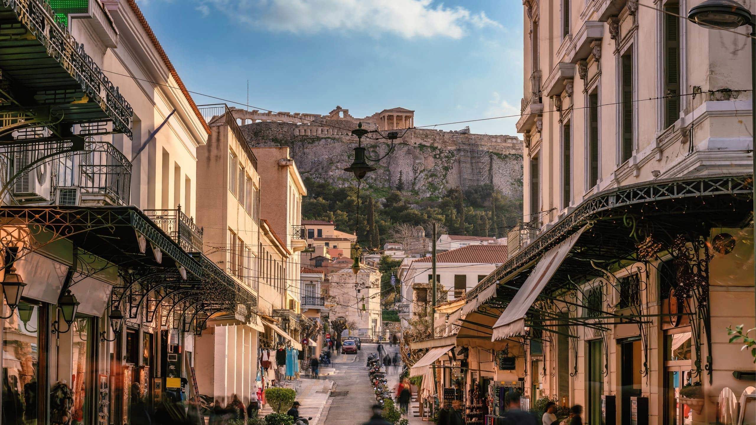 A lively street in Athens leads towards the Acropolis, with historic buildings, local shops and the ancient hilltop landmark in the distance - Greece: Ancient Wonders Tour