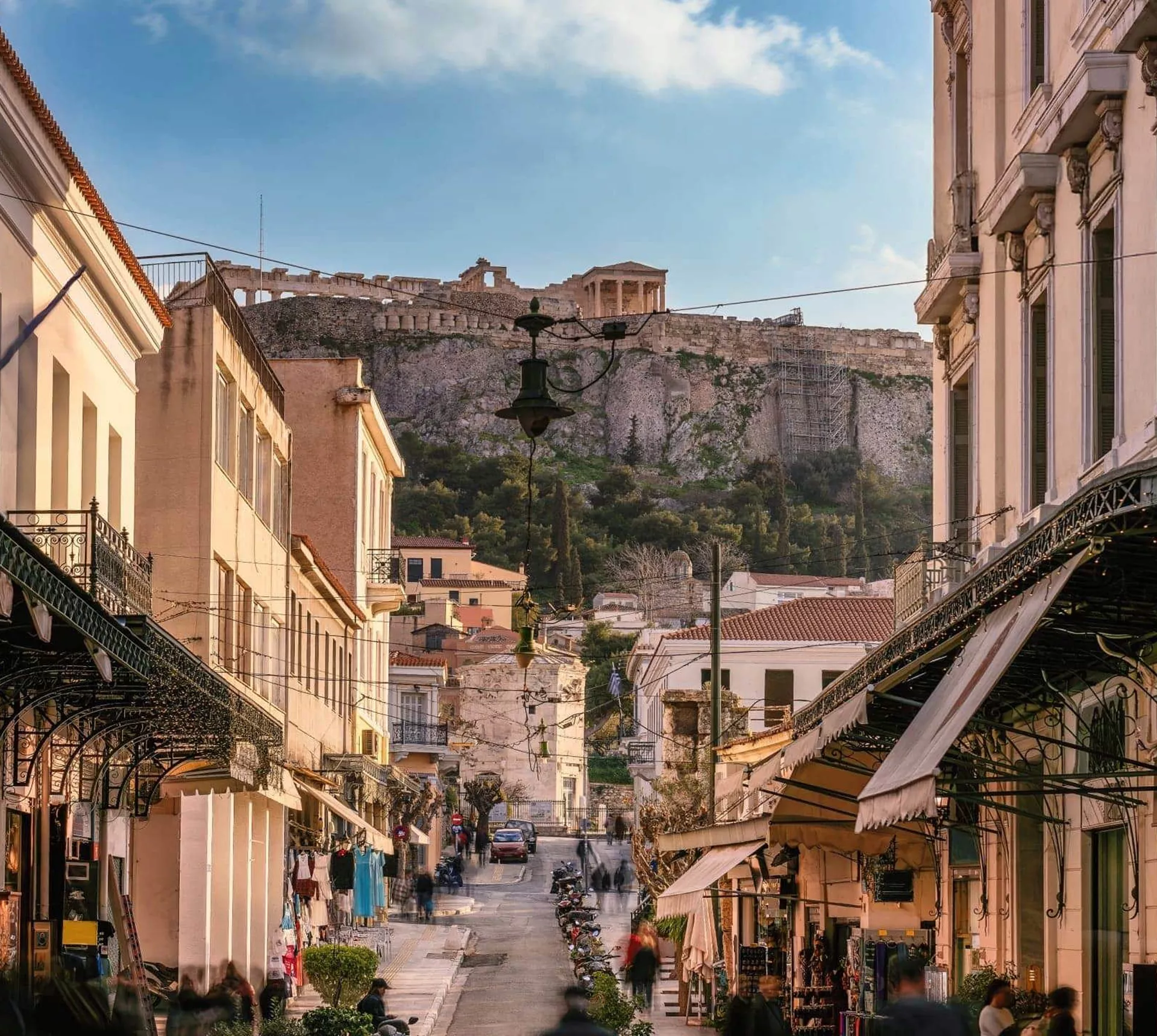 A lively street in Athens leads towards the Acropolis, with historic buildings, local shops and the ancient hilltop landmark in the distance - Greece: Ancient Wonders Tour
