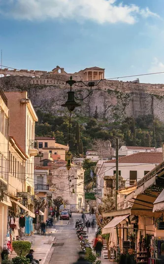 A lively street in Athens leads towards the Acropolis, with historic buildings, local shops and the ancient hilltop landmark in the distance - Greece: Ancient Wonders Tour