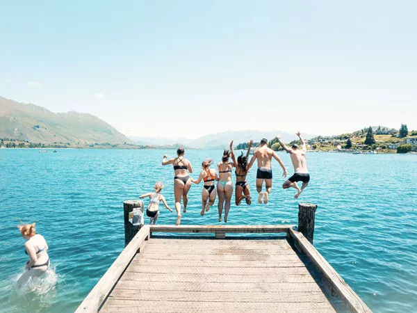 Group Of Friends Jumping Off Into Lake Mountains Around The Lake