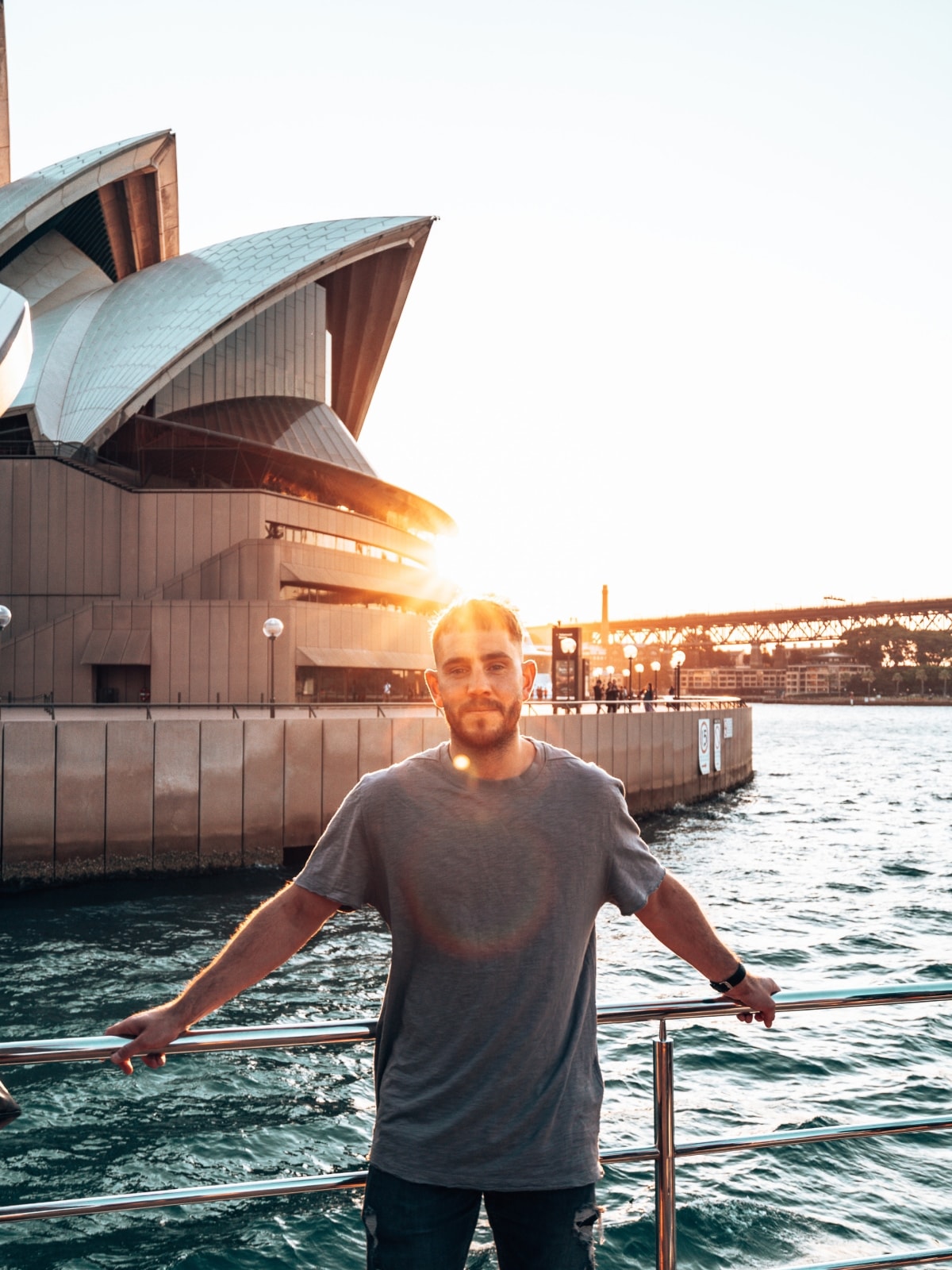 Traveller standing beside Sydney Opera House at sunset on Sydney Harbour, Australia.