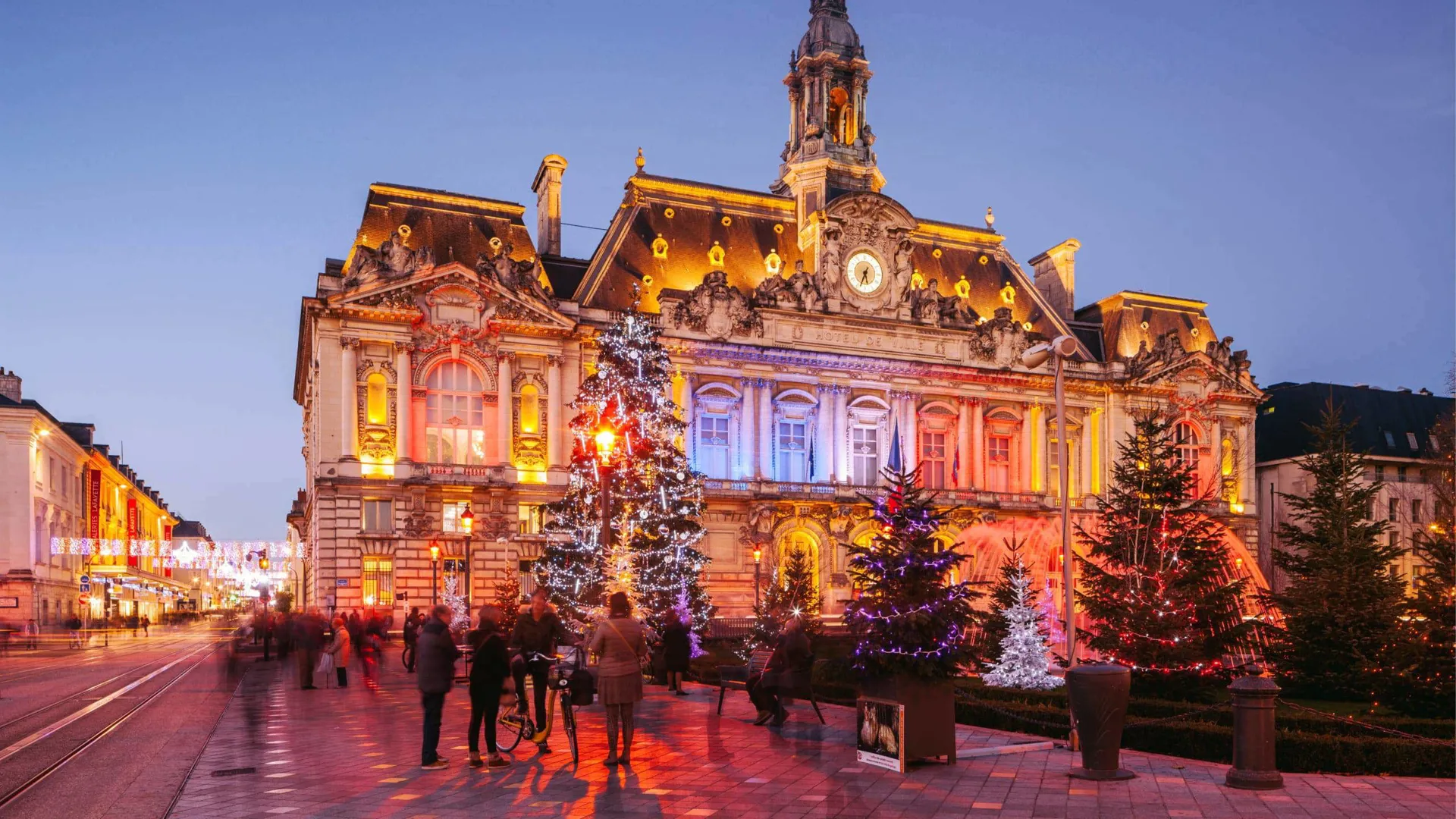 Contiki travellers exploring a stunning Christmas market square in Paris with a illuminated baroque town hall and decorated Christmas trees at twilight