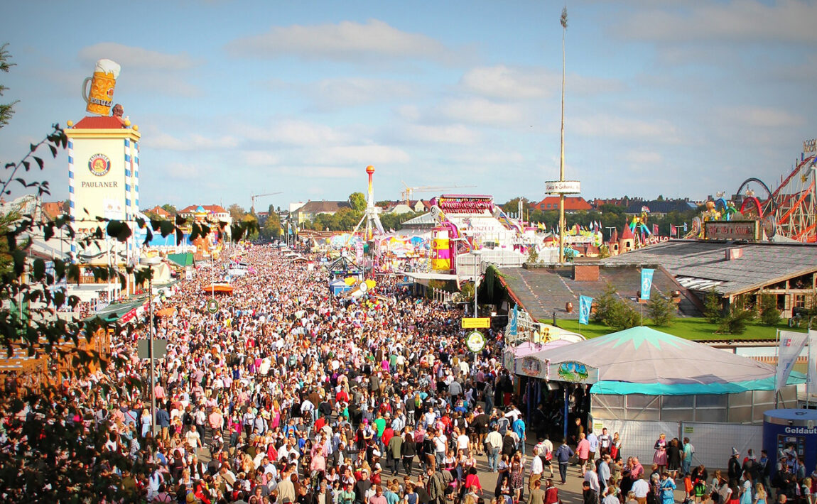 A crowd of people at an amusement park during Oktoberfest.
