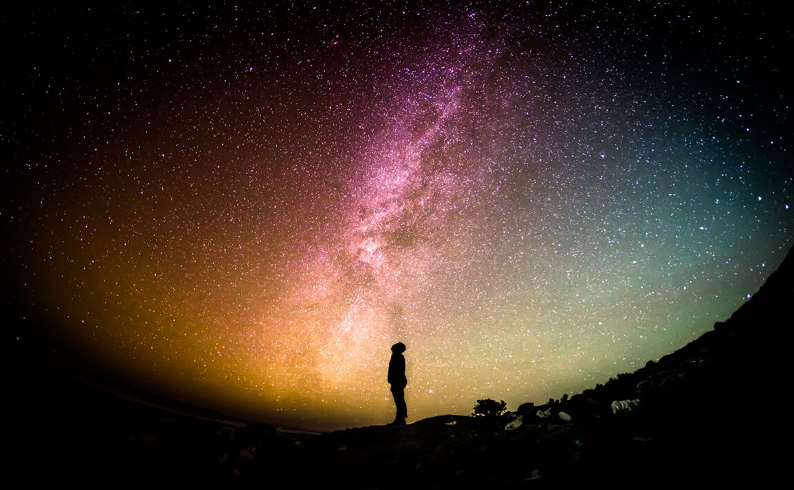 A person standing on a rock gazing up at the milky way, experiencing astrotourism.