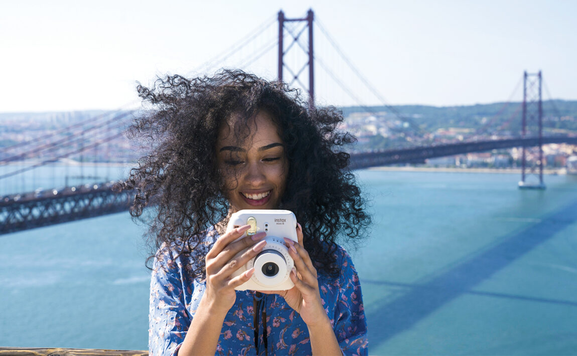 A woman is taking a picture with her camera in front of a bridge, showcasing one of the safest countries to travel solo.