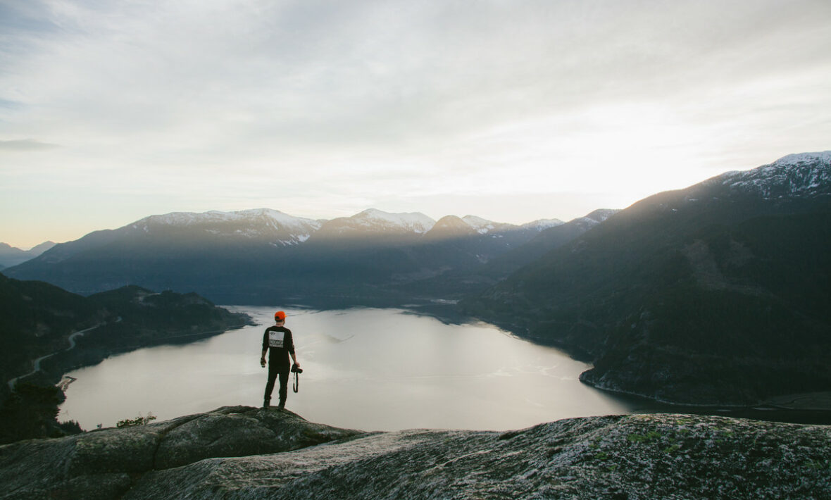 One of the best places to travel alone - a person standing on top of a mountain overlooking a lake.