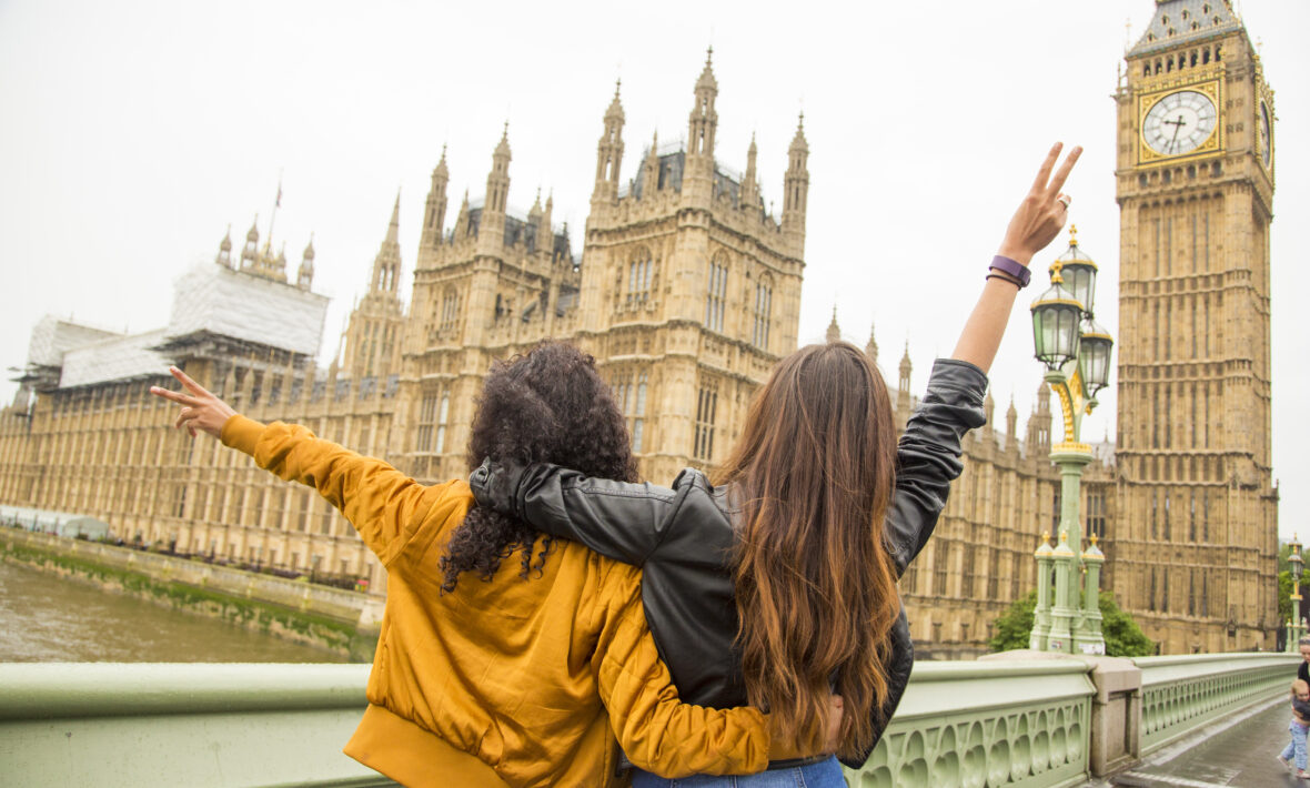 Two women waving in front of the Houses of Parliament