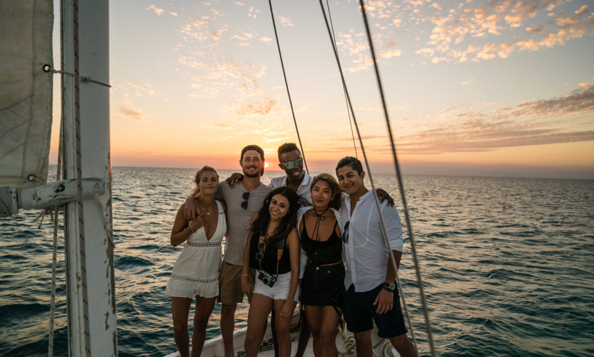 Young people standing on sailboat foredeck at sunset