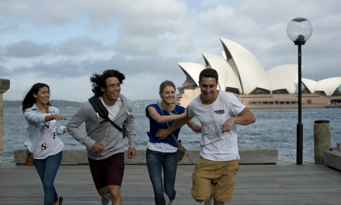 A group of people running on a pier beside the stunning Sydney Opera House, with mesmerizing views of beaches and reefs in the background.