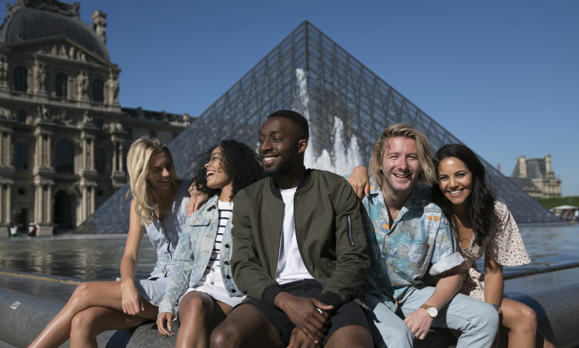 A group of Contiki age people posing in front of the Louvre pyramid.