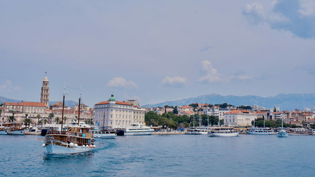 A boat sailing near a city in Croatia with mountains in the background.