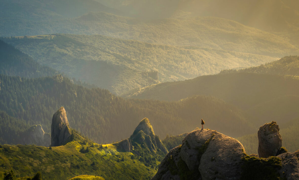 A person is standing on top of a rock, feeling inspired by the vastness of travel and adventures.