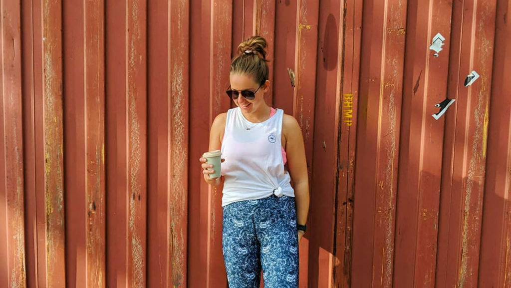 A woman's side hustle involves standing in front of a red wall holding a cup of coffee.