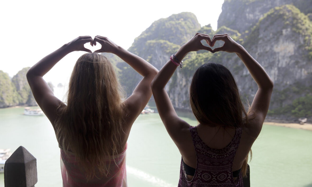 Two women using dating apps and making a heart shape with their hands.