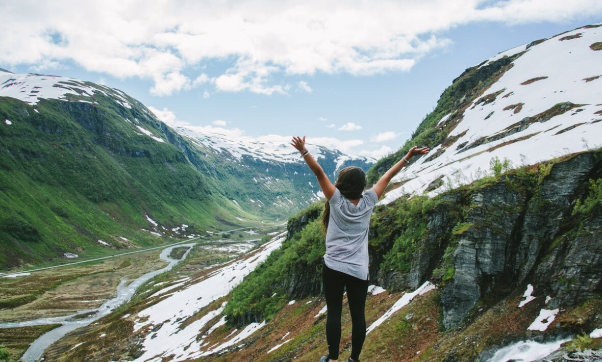 A woman standing on top of a mountain in the happiest country in the world with her arms raised.