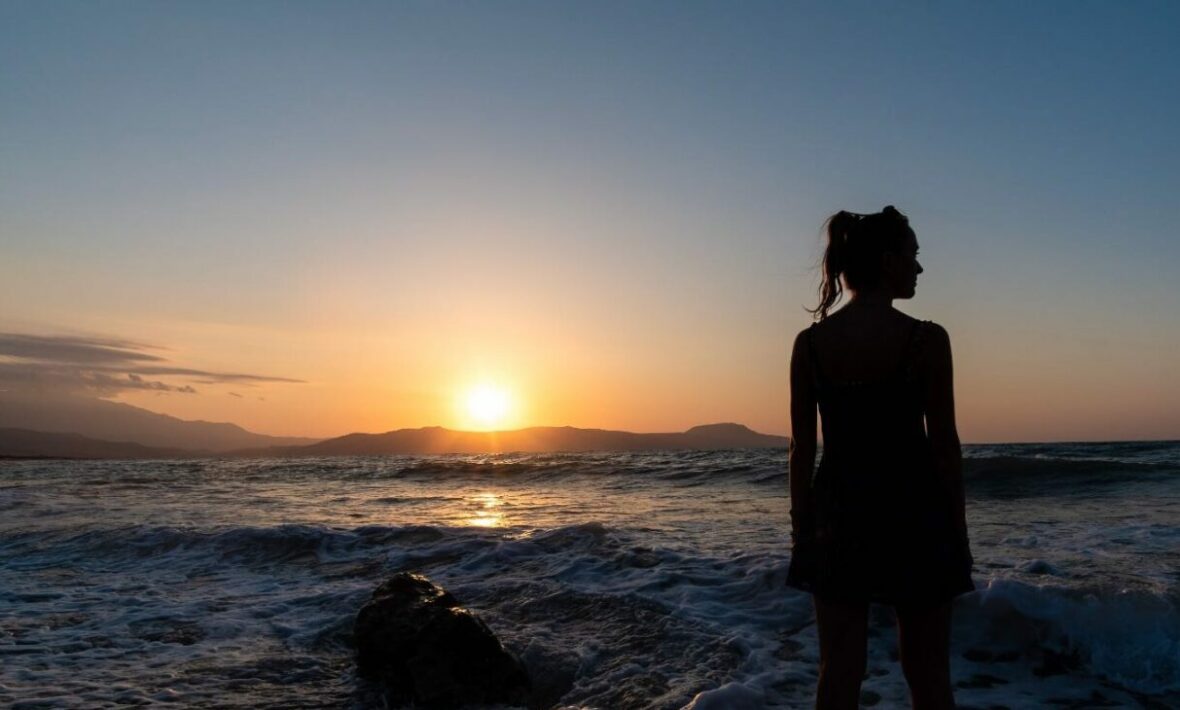 A silhouette of a woman standing on the beach at sunset.