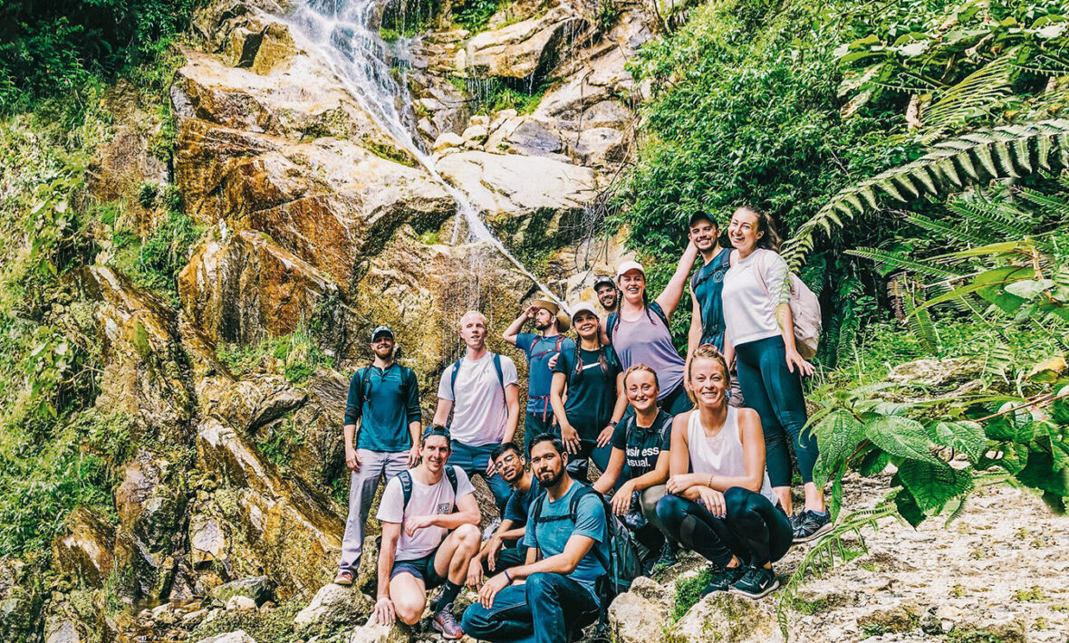 A group of people travelling and posing in front of a waterfall.