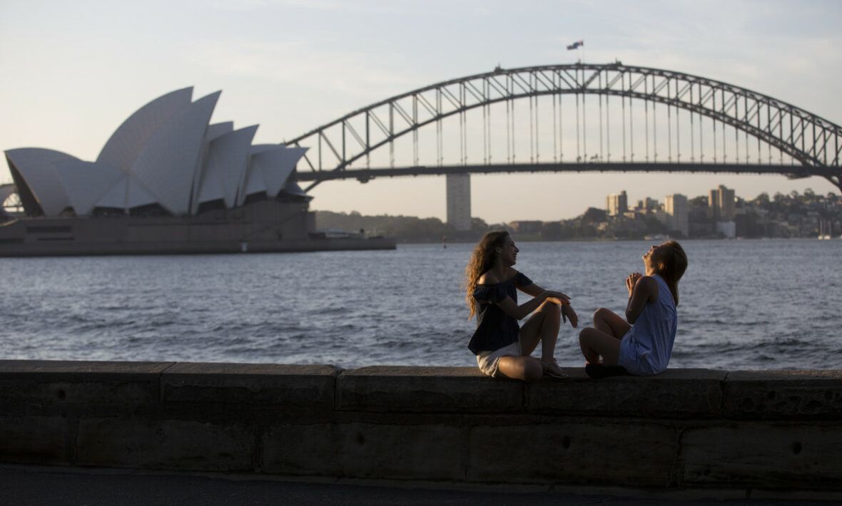 Two women sitting on a wall in front of the Sydney Opera House, job-inspired move.