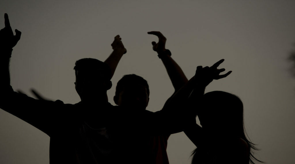 Silhouette of a group of people with their hands raised in the air, captivated by trance music.