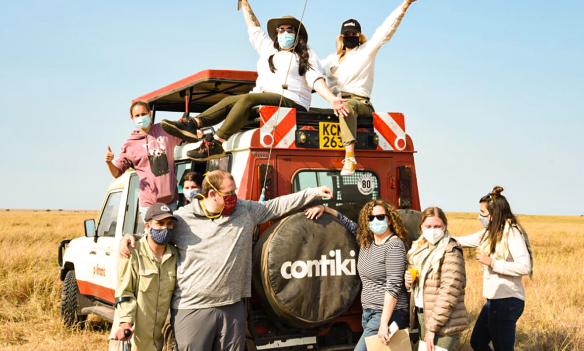 A group of people standing on top of a truck during an African safari experience in the middle of a field.