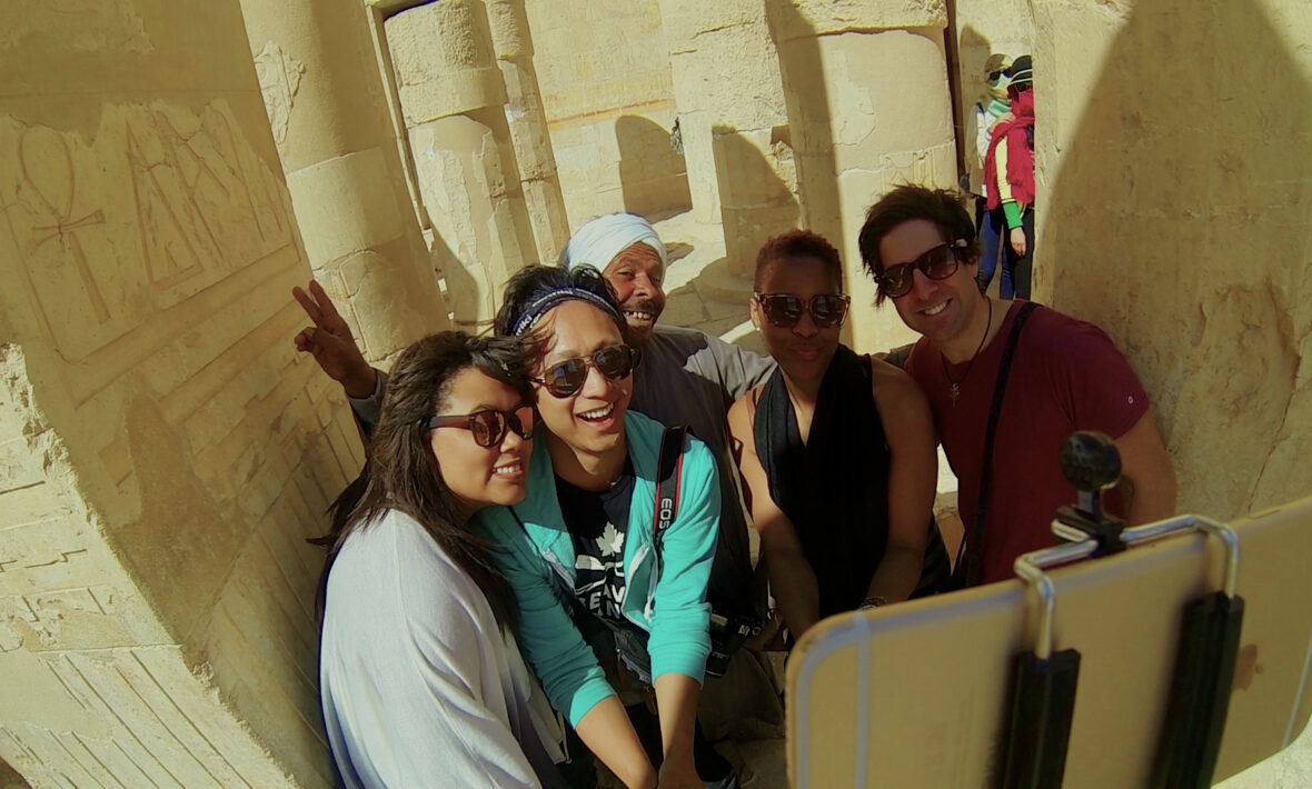 A group of people are posing for a photo in front of a ancient egyptian temple during their travels.