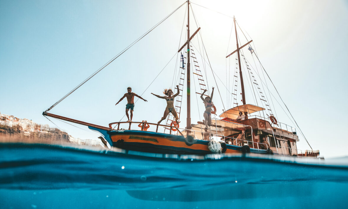 Friends jumping off boat into water having fun in Europe