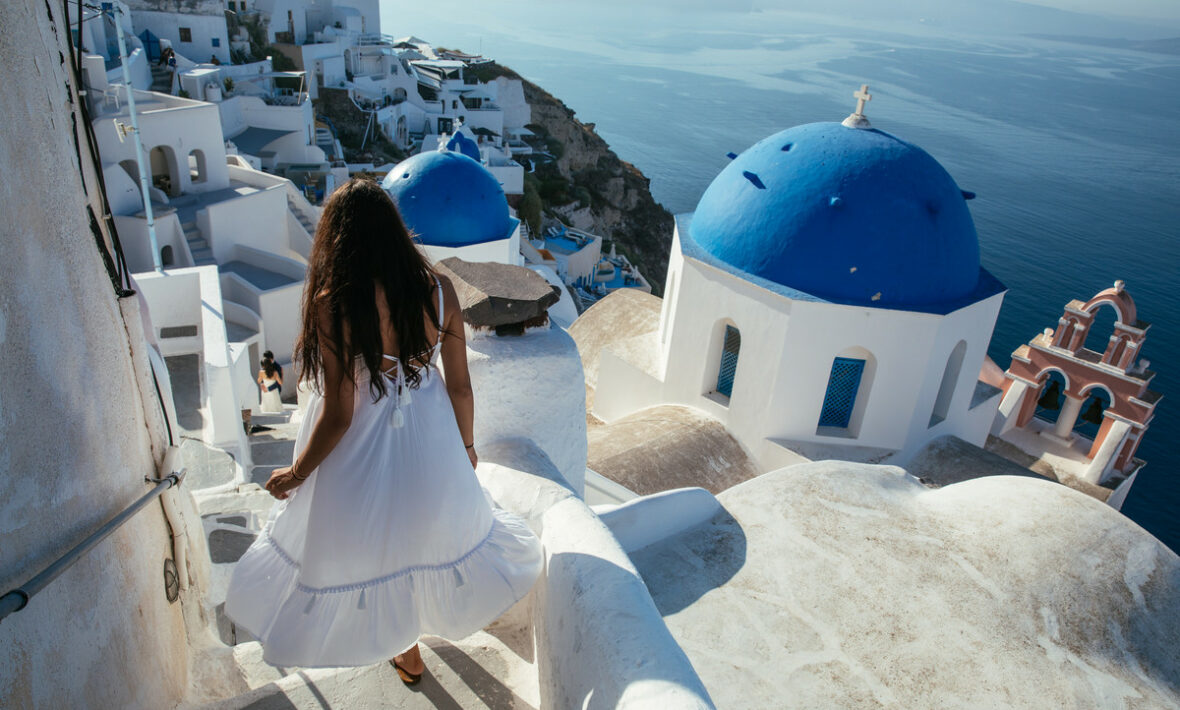 A woman in a white dress walking down the stairs in Santorini, Greece promotes brain health.