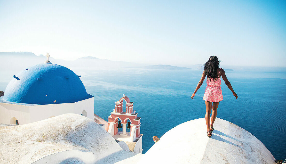 A woman is solo travelling on top of a hill overlooking the ocean.