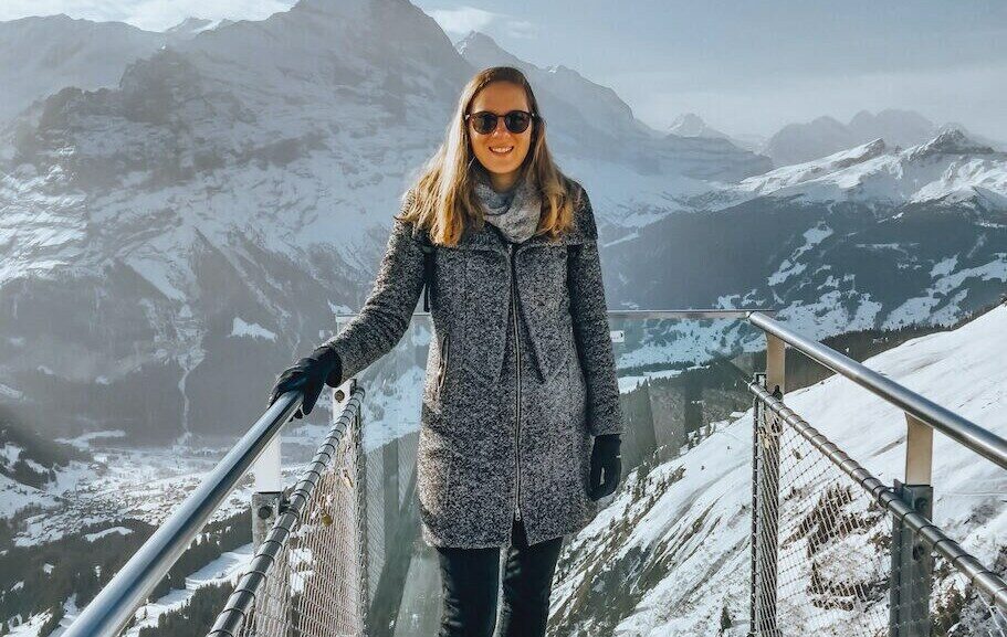 A woman embracing world tourism day, standing on a railing overlooking a snowy mountain.