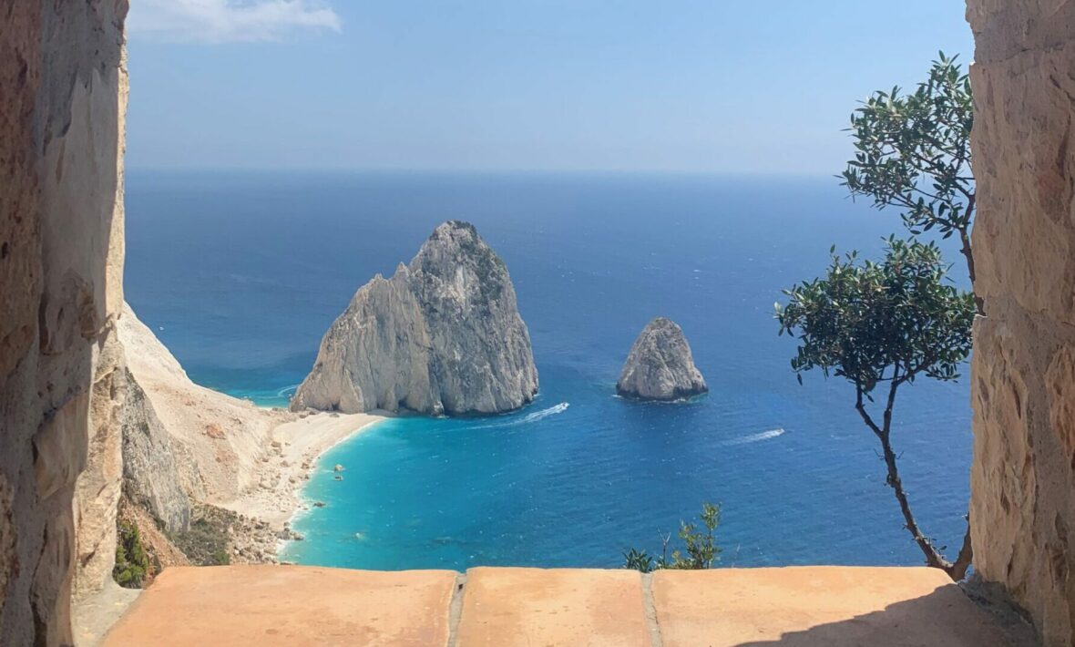 A view of a beach from a window in an old building with Greek food.