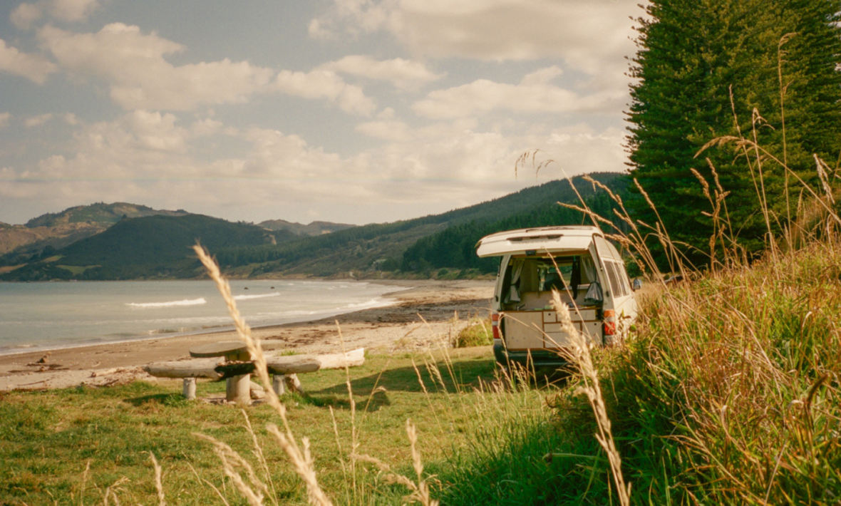 A camper van parked on a grassy hill next to the ocean.