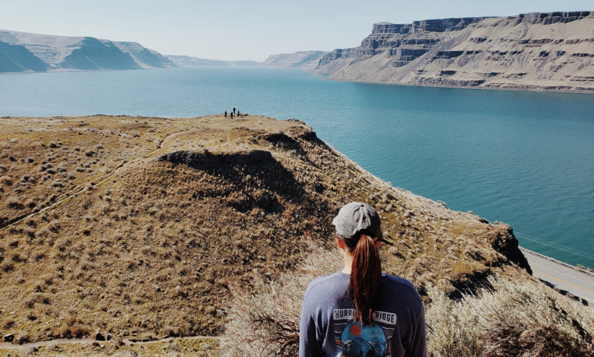 A woman is standing on a cliff overlooking a body of water.