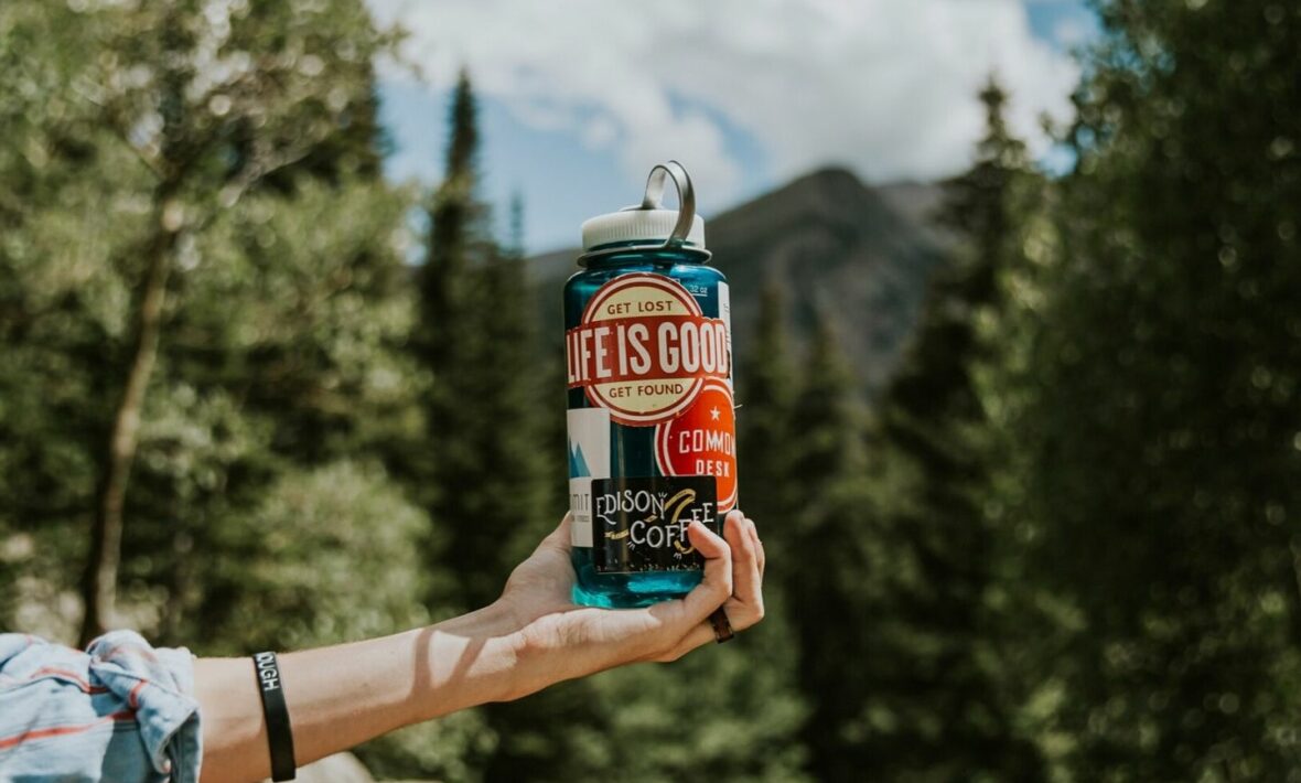 A person holding up a blue water bottle with sustainable travel tips in the background.