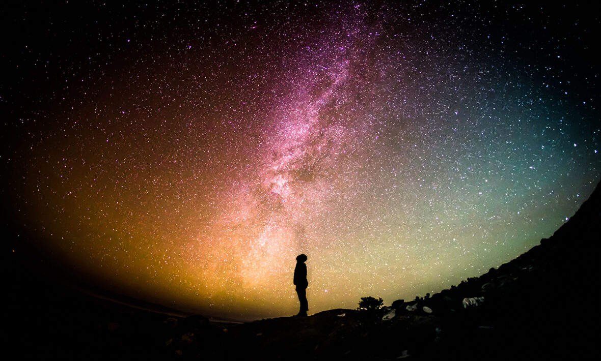 A person standing on a rock gazing up at the milky way, experiencing astrotourism.