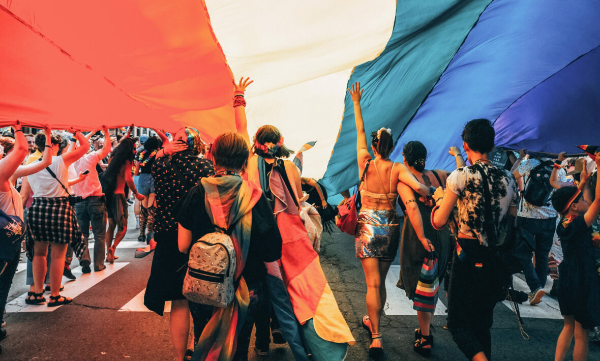 A group of LGBTQ+ individuals holding a rainbow flag in Spain.